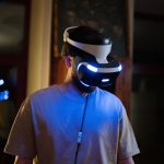 A young man using a VR headset in a dimly lit room indoors, showcasing virtual reality technology.